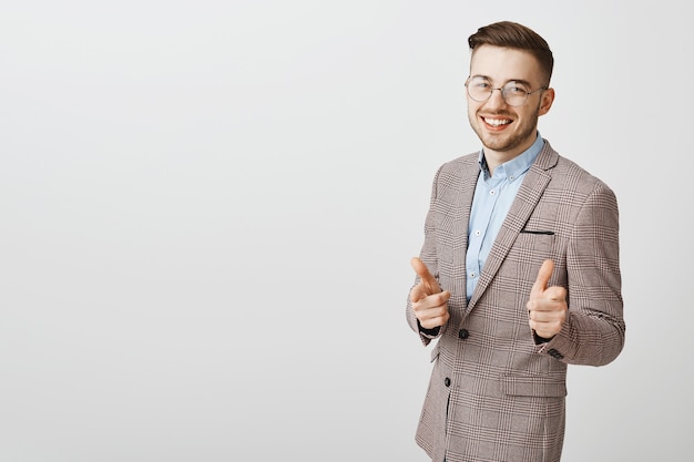 Hombre de negocios feliz y confiado señalando pistolas con el dedo y sonriendo complacido, elogia el buen trabajo, felicita a alguien, dice felicidades