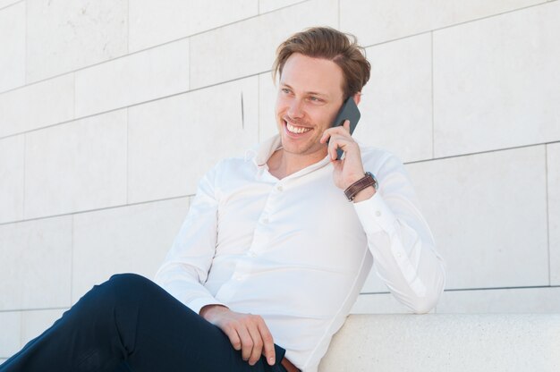 Hombre de negocios feliz llamando a smartphone en banco al aire libre