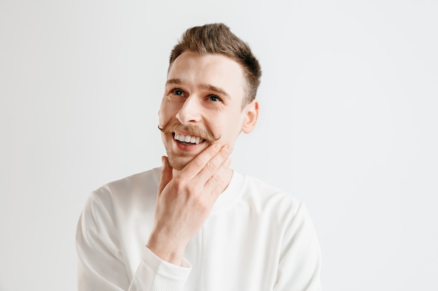 Hombre de negocios feliz de pie, sonriendo aislado sobre fondo gris de estudio. Hermoso retrato masculino de medio cuerpo. Joven satisface al hombre. Las emociones humanas, el concepto de expresión facial.