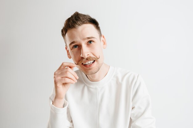 Hombre de negocios feliz de pie, sonriendo aislado sobre fondo gris de estudio. Hermoso retrato masculino de medio cuerpo. Joven satisface al hombre. Las emociones humanas, el concepto de expresión facial.