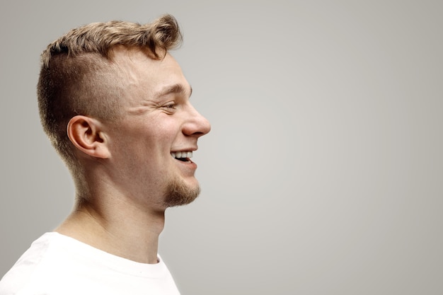 Hombre de negocios feliz de pie, sonriendo aislado sobre fondo gris de estudio. Hermoso retrato de perfil masculino. Joven satisface al hombre. Las emociones humanas, el concepto de expresión facial.