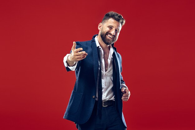 El hombre de negocios feliz de pie y sonriendo contra la pared roja