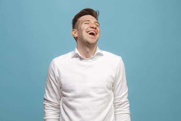 Hombre de negocios feliz de pie y sonriente aislado sobre fondo azul de estudio. Hermoso retrato masculino de medio cuerpo. Joven emocional. Las emociones humanas, el concepto de expresión facial. Vista frontal.