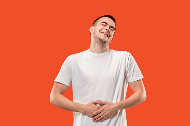 El hombre de negocios feliz de pie y sonriente contra la pared de color naranja.