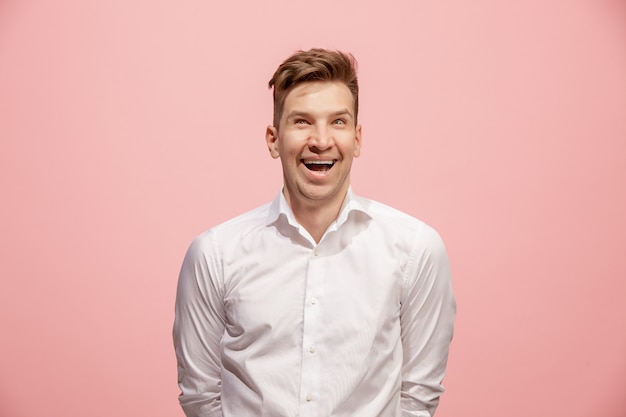 El hombre de negocios feliz de pie y sonriente contra la pared de color rosa.