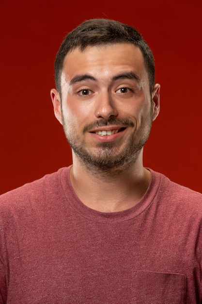 El hombre de negocios feliz de pie y sonriente contra la pared roja.