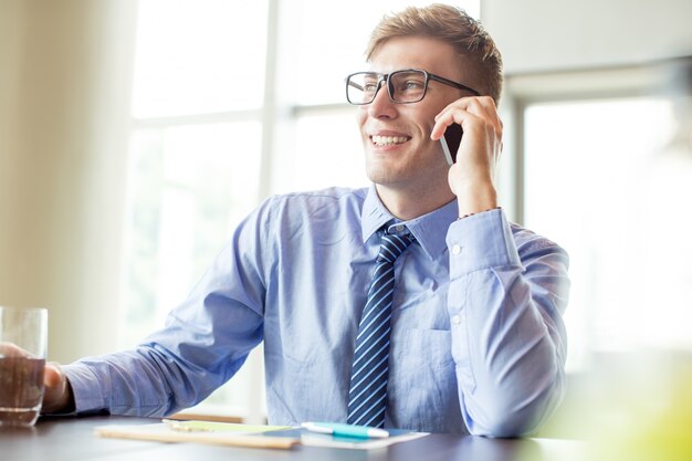 Hombre de negocios feliz que llama en el teléfono en la mesa de la oficina