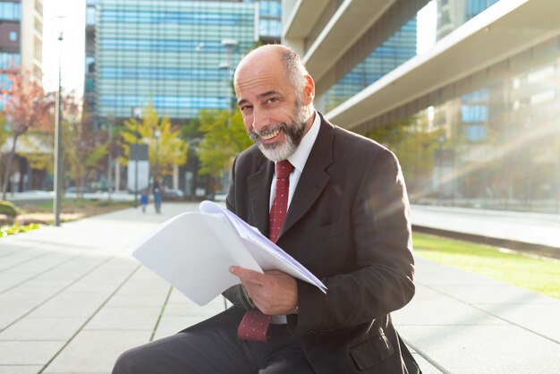 Hombre de negocios feliz que sostiene los papeles al aire libre