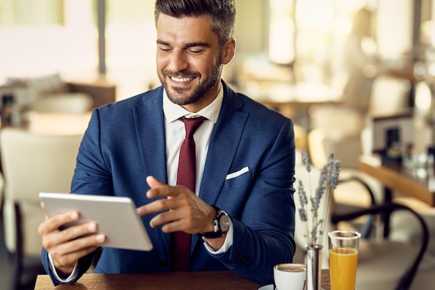 Hombre de negocios feliz que usa la tableta digital en un café