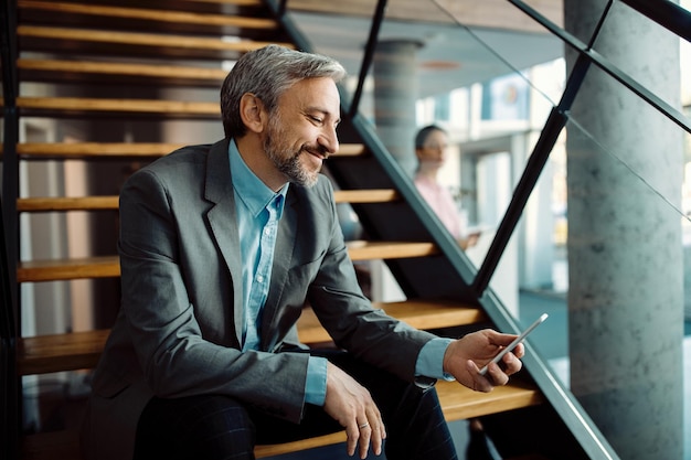 Hombre de negocios feliz que usa el teléfono móvil mientras se relaja en la escalera