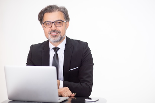 Hombre de negocios feliz sentado a la mesa con la computadora portátil