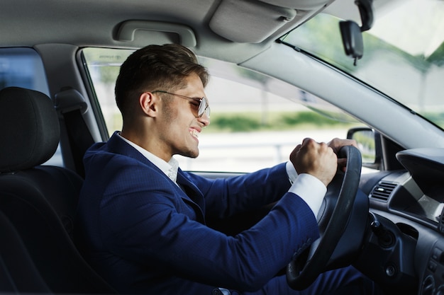 El hombre de negocios feliz se sienta muestra sus emociones que se sientan en el volante dentro del coche