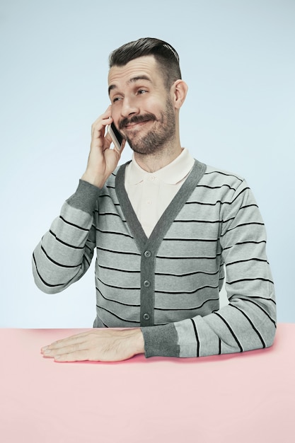 Foto gratuita hombre de negocios feliz sonriente hablando por teléfono sentado en la mesa. concepto de emociones masculinas
