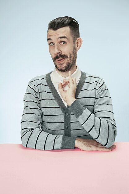 El hombre de negocios feliz, sonriente, loco y divertido sentado a la mesa en el espacio azul