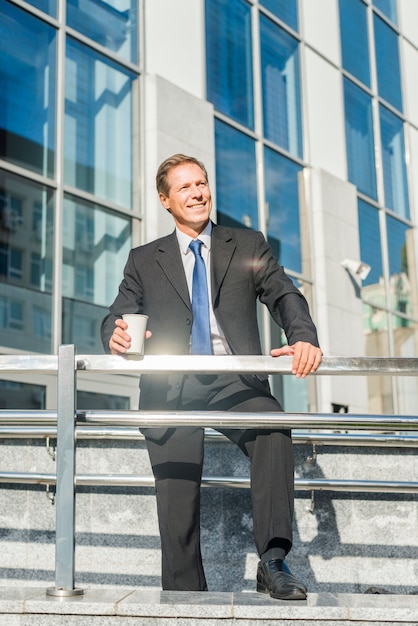 Hombre de negocios feliz con la taza de café que se coloca delante del edificio
