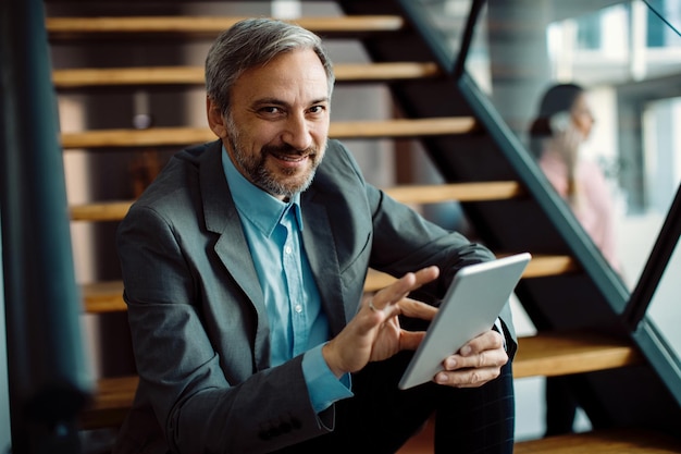 Foto gratuita hombre de negocios feliz usando el panel táctil mientras se relaja en la escalera y mira la cámara