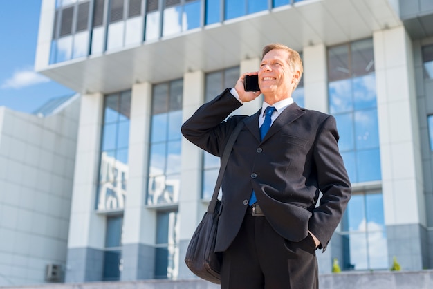 Hombre de negocios feliz usando el teléfono móvil en frente del edificio