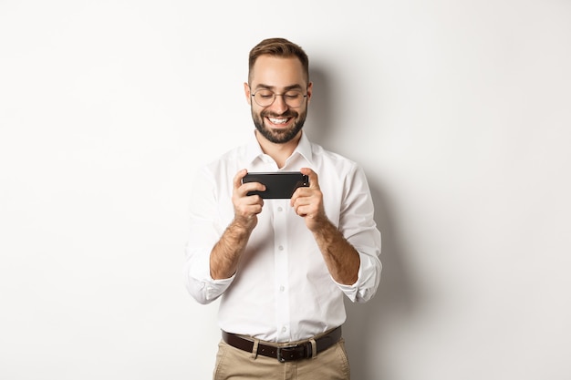 Hombre de negocios feliz viendo videos en el teléfono móvil, de pie.