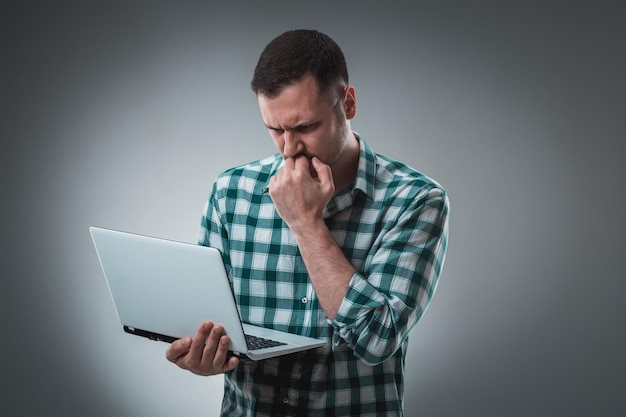 Foto gratuita un hombre de negocios frustrado con una computadora portátil cubre su cara con su mano sobre un fondo gris.