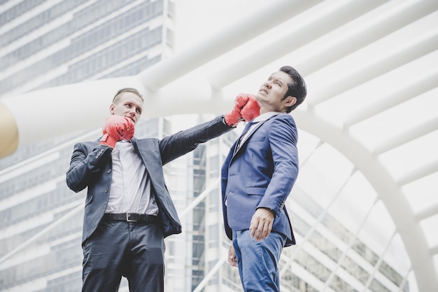 Hombre de negocios con los guantes de boxeo rojos listos para luchar a su compañero de trabajo.