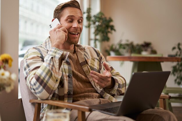 Hombre de negocios guapo en una cafetería sentado en una cafatería con una computadora portátil y llamando a alguien hombre hablando en