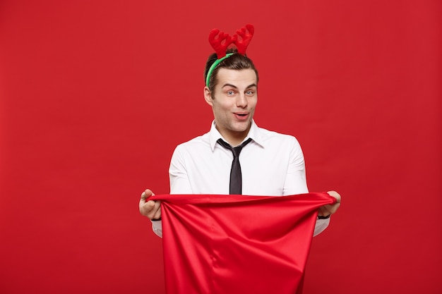 Hombre de negocios guapo celebrar feliz Navidad con diadema de renos con bolsa grande roja de Santa.