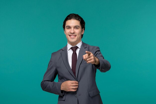 Hombre de negocios guapo chico lindo en traje de oficina gris sonriendo y apuntando al frente