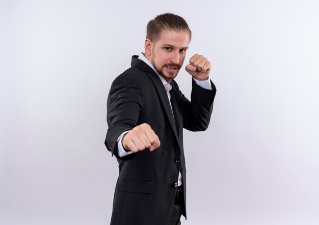 Hombre de negocios guapo frustrado vistiendo traje apretando los puños posando como boxeador de pie sobre fondo blanco.