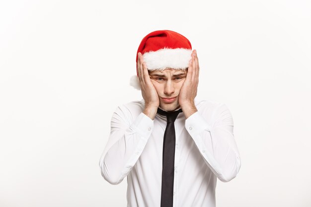 Hombre de negocios guapo con sombrero de santa posando con estresante expresión facial en blanco.