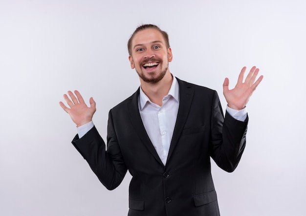 Hombre de negocios guapo vestido con traje levantando las palmas de las manos feliz y positivo sonriendo alegremente de pie sobre fondo blanco.