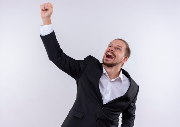 Hombre de negocios guapo vestido con traje levantando el puño loco feliz de pie sobre fondo blanco.