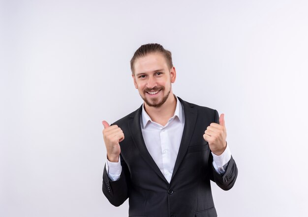 Hombre de negocios guapo vestido con traje loco feliz mostrando los pulgares para arriba sobre fondo blanco.