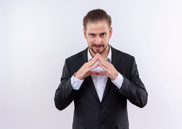 Hombre de negocios guapo vestido con traje mirando a la cámara con expresión de confianza tomados de la mano juntos de pie sobre fondo blanco.