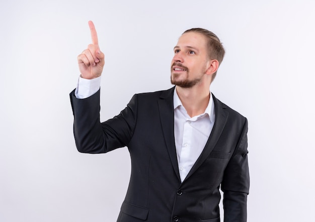 Foto gratuita hombre de negocios guapo vestido con traje mirando a un lado apuntando hacia arriba con el dedo índice de pie sobre fondo blanco.