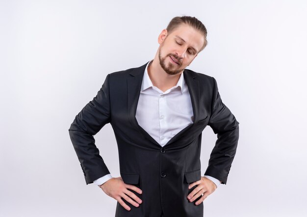 Hombre de negocios guapo vestido con traje mirando a un lado con expresión de confianza de pie sobre fondo blanco.