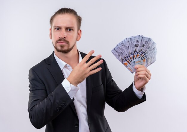 Hombre de negocios guapo vestido con traje mostrando dinero en efectivo mirando a la cámara con rostro serio mostrando el número cuatro de pie sobre fondo blanco.