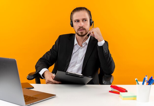 Hombre de negocios guapo vestido con traje de pie sobre fondo naranja