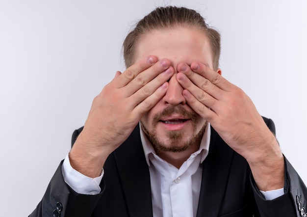 Foto gratuita hombre de negocios guapo vestido con traje que cubre los ojos con los brazos de pie sobre fondo blanco.