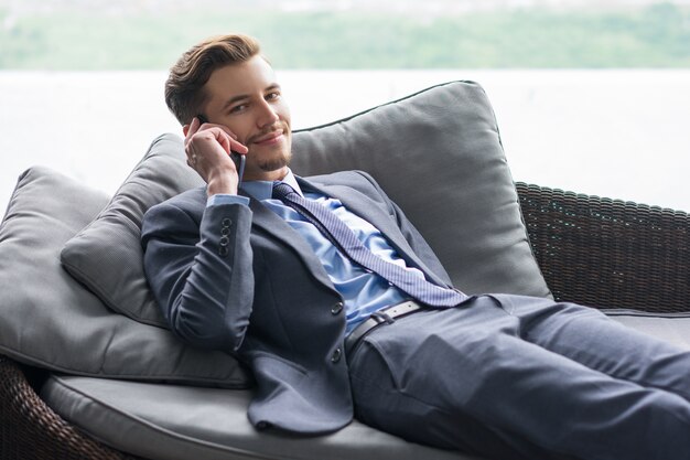 El hombre de negocios hablando por teléfono tirado en el sofá sonriendo