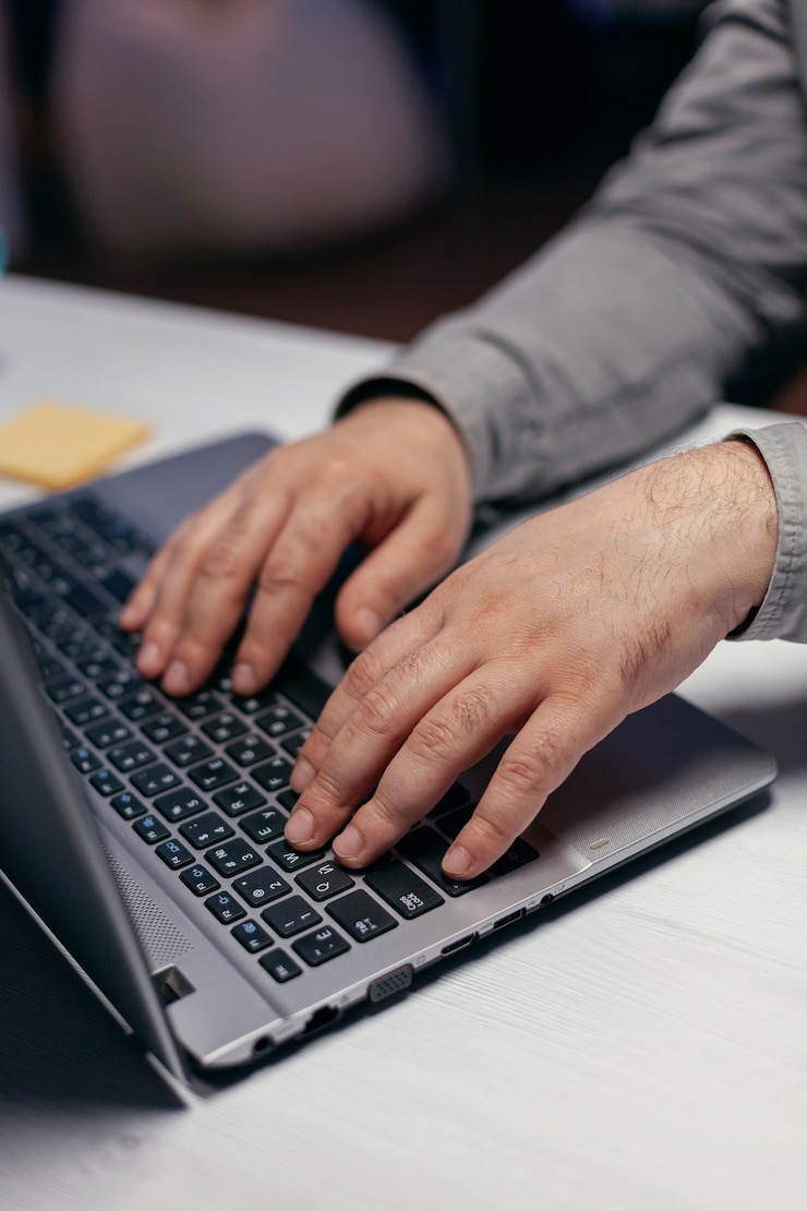 Foto gratuito hombre de negocios haciendo multitarea en la oficina oscura. cerca de manos masculinas escribiendo en el teclado de la computadora portátil en la oficina. negocios, trabajando desde casa, estudiando el concepto en línea