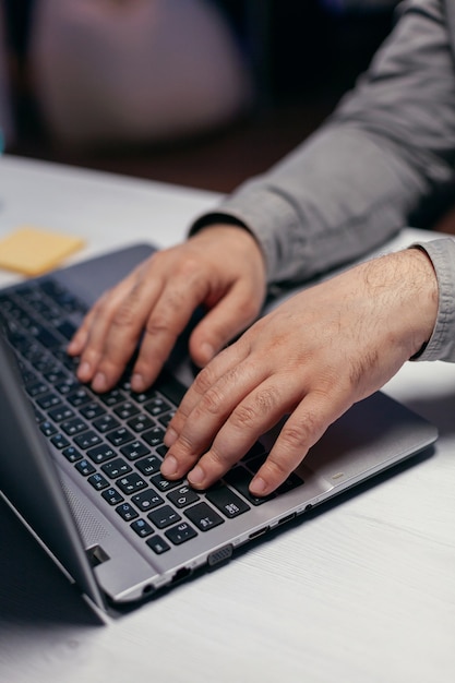 Hombre de negocios haciendo multitarea en la oficina oscura. Cerca de manos masculinas escribiendo en el teclado de la computadora portátil en la oficina. Negocios, trabajando desde casa, estudiando el concepto en línea