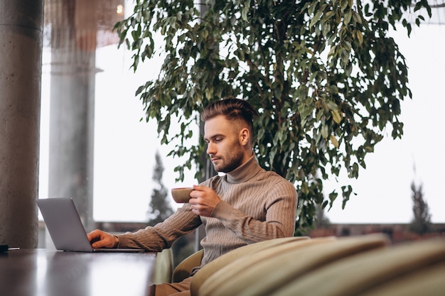 Hombre de negocios hermoso que trabaja en la computadora y que bebe el café en un café