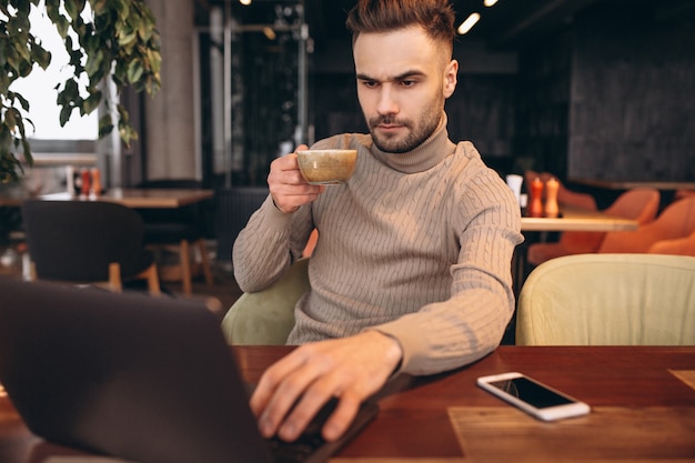 Hombre de negocios hermoso que trabaja en la computadora y que bebe el café en un café