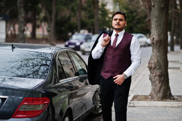 Hombre de negocios indio con estilo en ropa formal de pie contra el coche de negocios negro en la calle de la ciudad