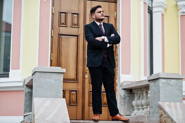 Hombre de negocios indio con estilo en ropa formal de pie contra la puerta en el centro de negocios con los brazos cruzados