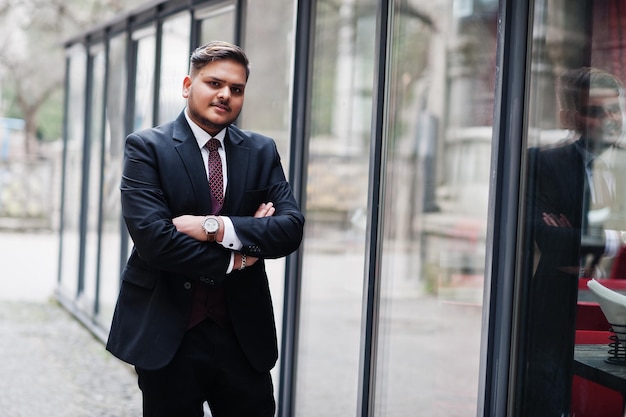 Hombre de negocios indio con estilo en ropa formal de pie contra las ventanas en el centro de negocios