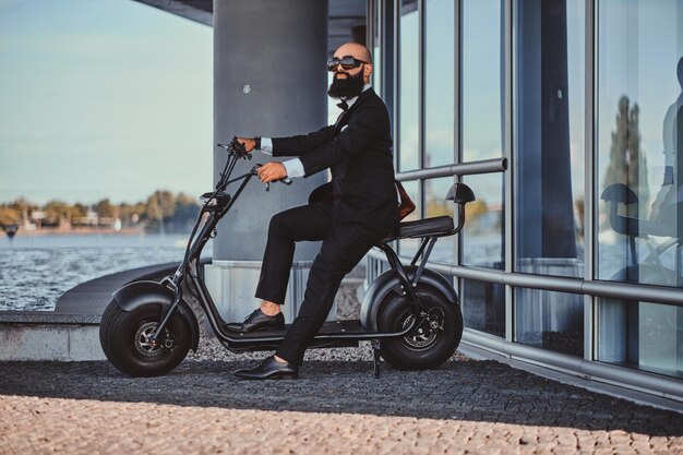 Un hombre de negocios inteligente y atractivo está sentado en su scooter eléctrico mientras posa para el fotógrafo.