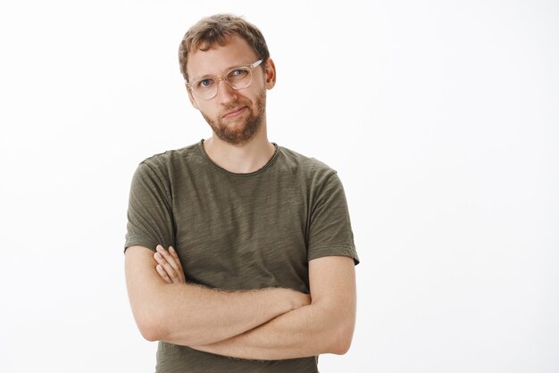 Hombre de negocios inteligente y creativo mandón disgustado con camiseta verde oscuro y gafas inclinando la cabeza y sonriendo de insatisfacción cruzando las manos sobre el pecho y disgustado el nuevo concepto