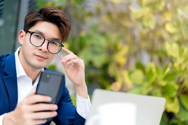 Hombre de negocios inteligente, traje formal, siéntese, relájese, sostenga el teléfono inteligente con una computadora portátil, televideoconferencia, reunión, trabajo remoto, distancia social, cerveza asiática, relájese en el fondo del parque del jardín.