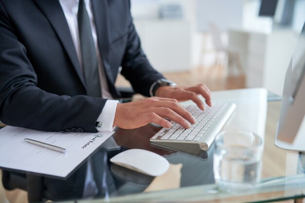 Hombre de negocios irreconocible escribiendo en el teclado en la oficina